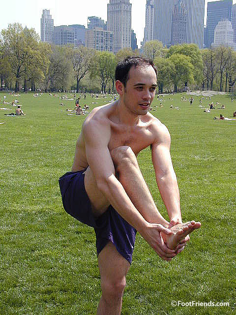 Amateur guy holding his own bare foot in the park