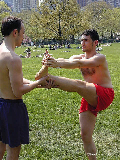 Guy helps his friend stretch barefoot